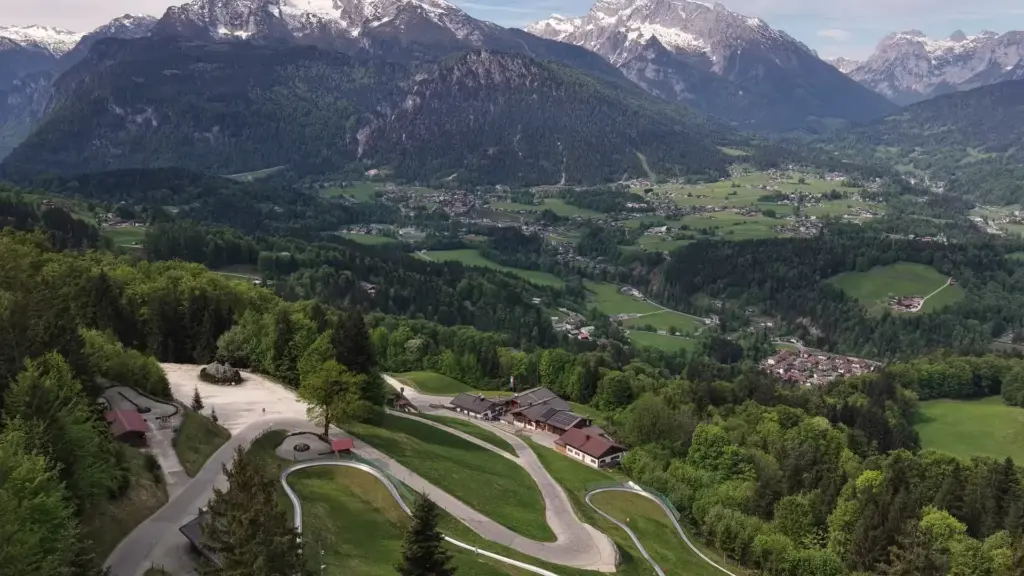 Luftbild: der Hochlenzer mit Parkplatz und Sommerrodelbahn am Waldrand, dahinter das Berchtesgadener Tal, Watzmann und Hochkalter