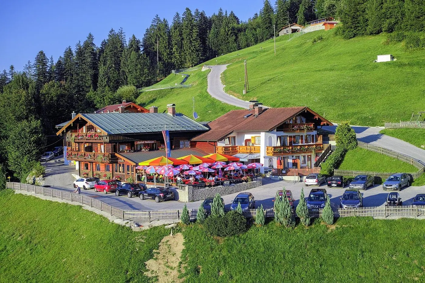 Der Hochlenzer mit bunten Sonnenschirmen auf der Terrasse und Parkplatz