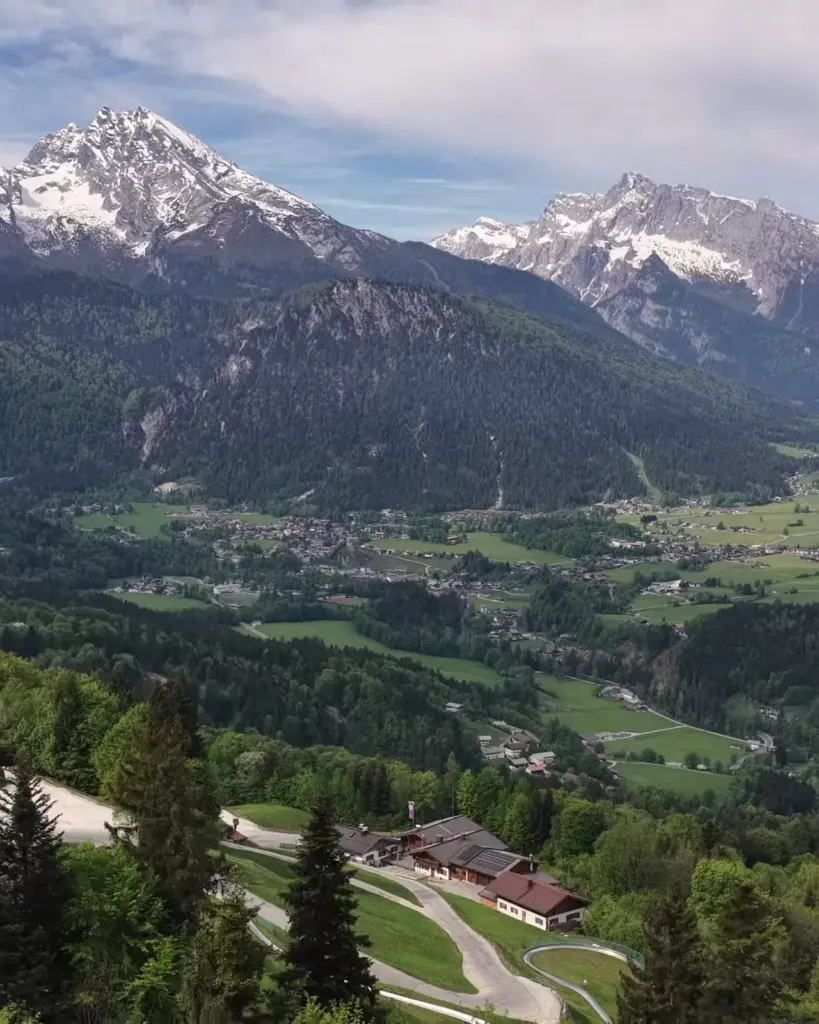 Luftbild: der Hochlenzer mit Rodelbahn am Waldrand, dahinter das Tal, Watzmann und Hochkalter