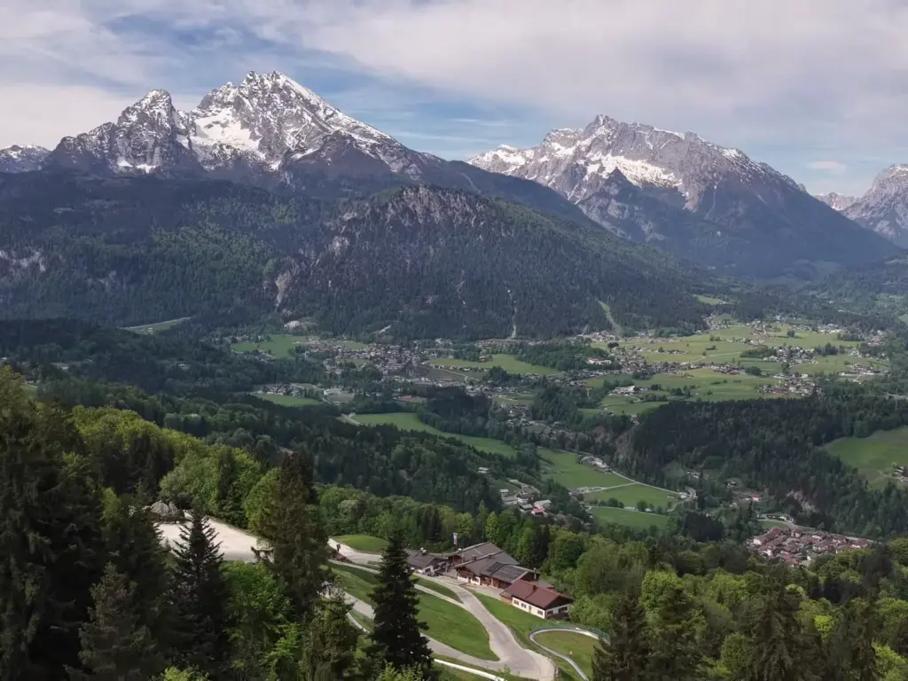 Luftbild: der Hochlenzer mit Rodelbahn am Waldrand, dahinter das Tal, Watzmann und Hochkalter