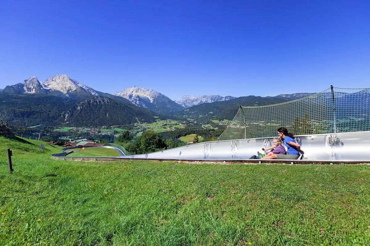 Mutter und Kind auf der Sommerrodelbahn, im Hintergrund der Watzmann