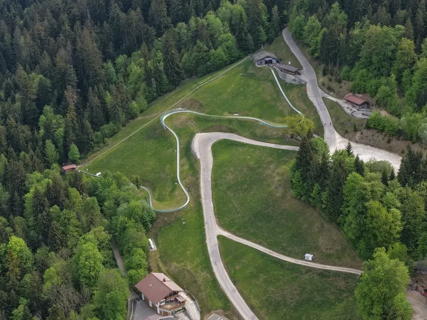 Luftbild der Almwiese oberhalb des Hochlenzer: die Sommerrodelbahn windet sich in Kehren den Hang hinunter, daneben der gerade Aufzug