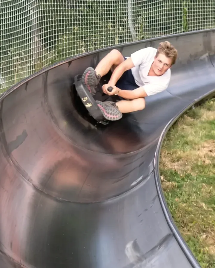 Junger Gast fährt mit dem Rodel durch die Steilkurve der Sommerrodelbahn